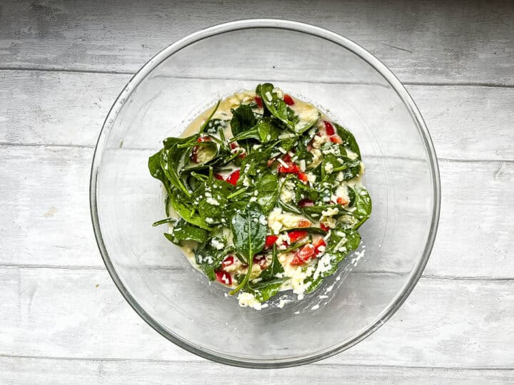 quiche egg and cheese mixture with spinach and red peppers in a bowl
