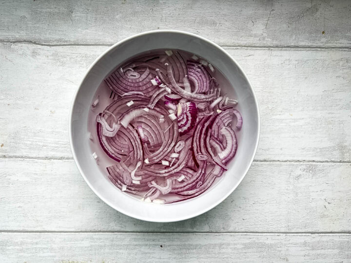 sliced red onions in bowl of ice water