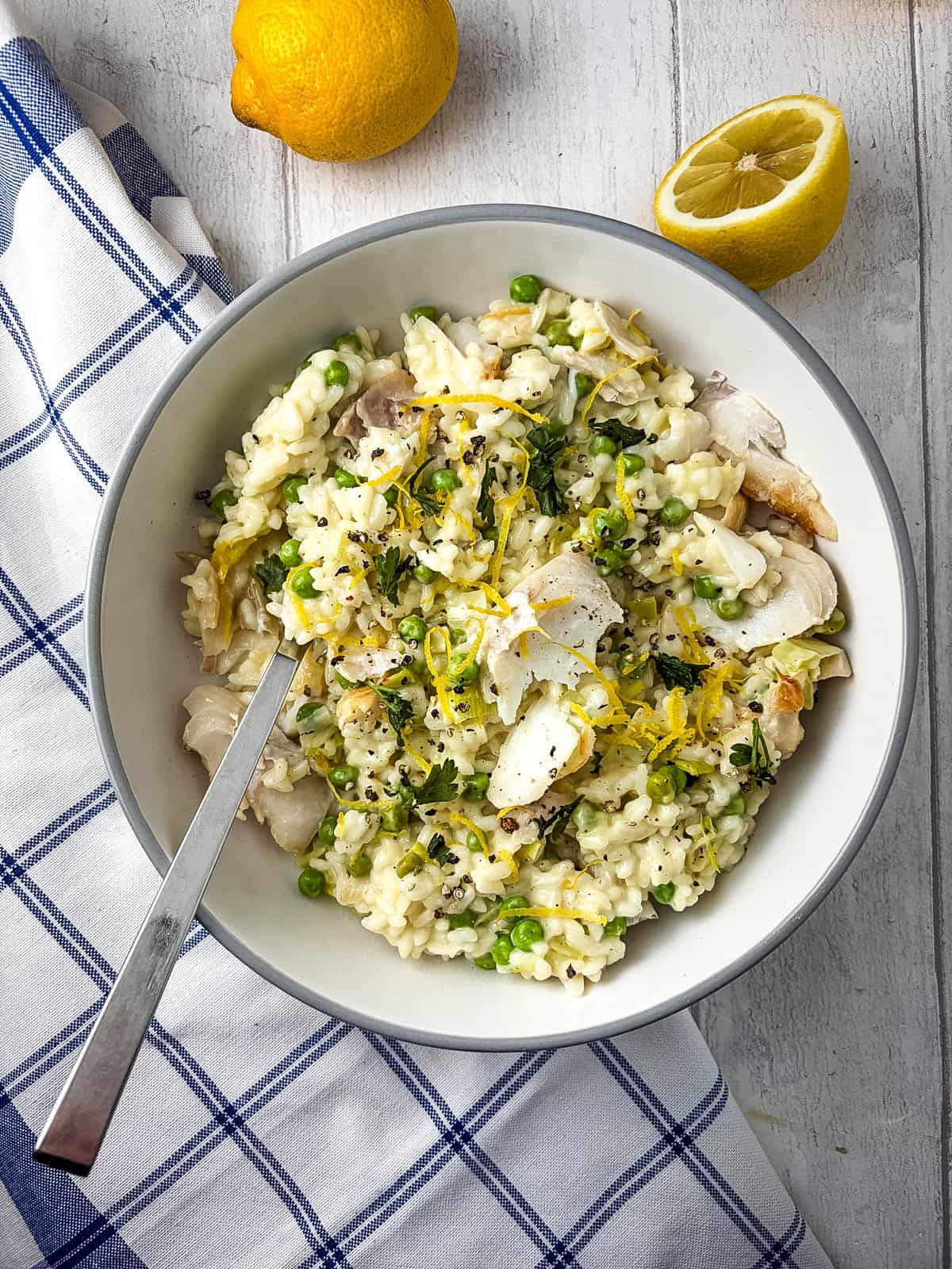 smoked haddock risotto in bowl with lemon zest and lemons lying to side of bowl.